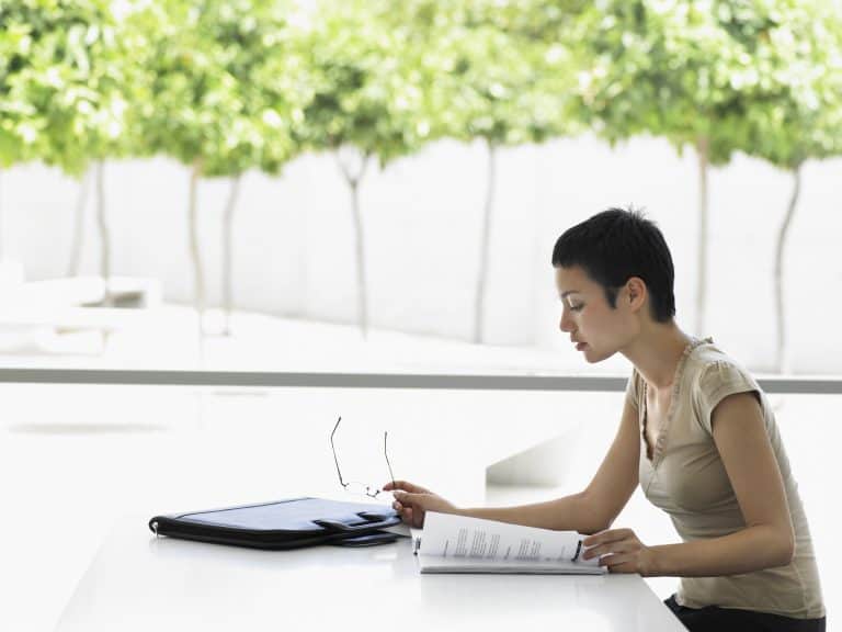 Woman reading documents at white table.