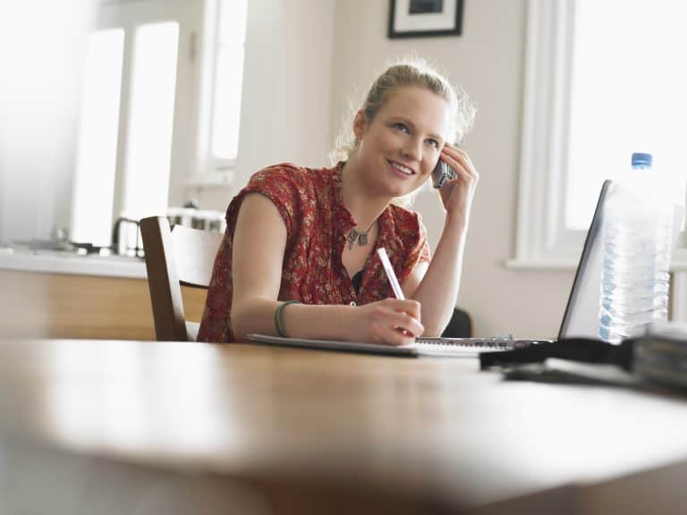 Woman writing and talking on phone at desk.