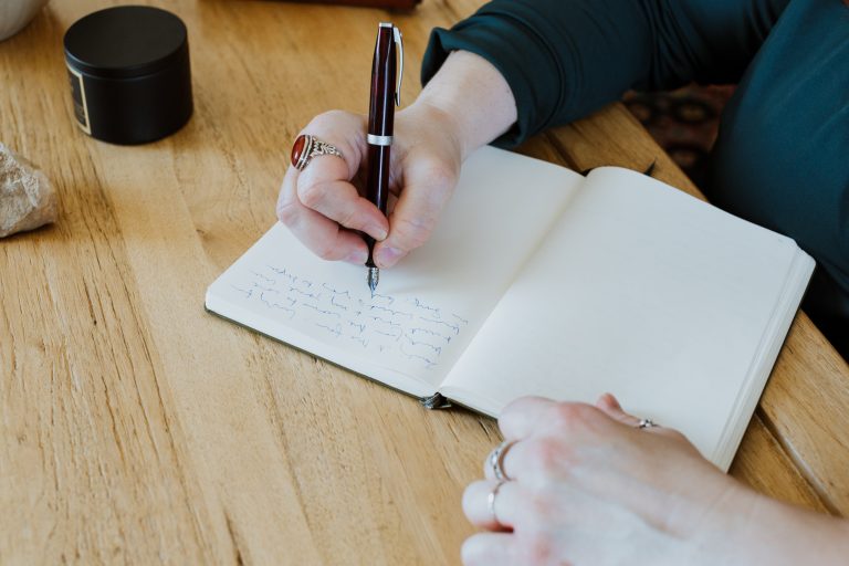 Person writing in notebook at wooden desk.