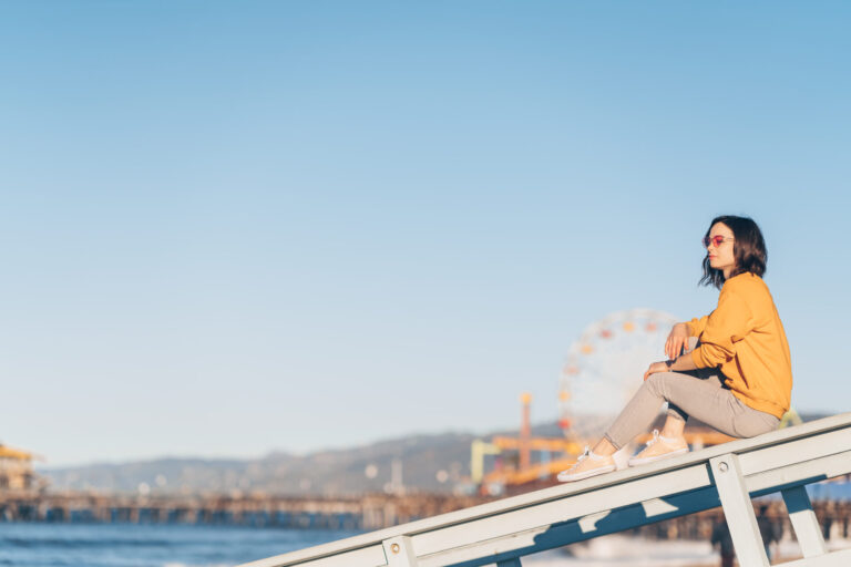 Woman sitting on pier, ferris wheel background.
