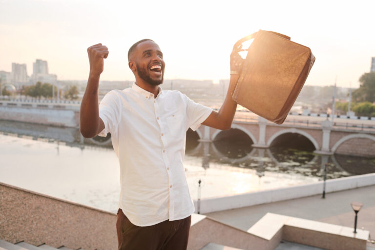 Cheerful man celebrating achievement with briefcase outdoors.