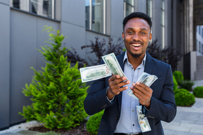 Smiling person holding cash outdoors.