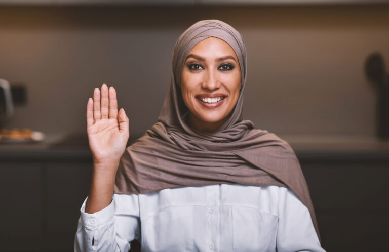 Smiling person in hijab waving hello.